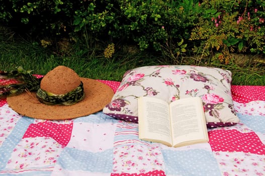 Relaxing in a garden with a blanket, straw hat, pillow and a book