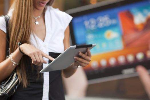 Young Woman with tablet computer walking on street, downtown. In background is blured advertisiment with OpenSource graphics. Visible noise