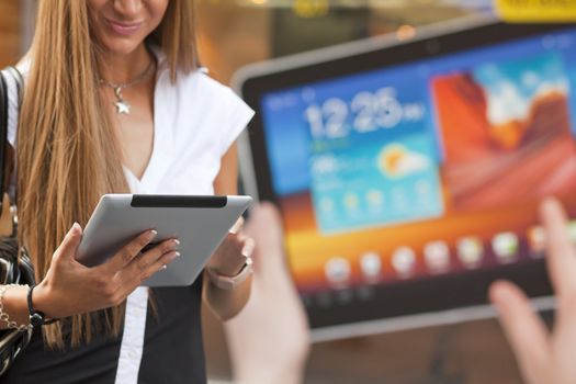Young Woman with tablet computer walking on street, downtown. In background is blured advertisiment with OpenSource graphics. Visible noise