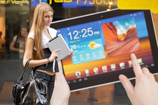 Young Woman with tablet computer walking on street, downtown. In background is blured advertisiment with OpenSource graphics. Visible noise