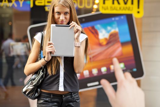 Young Woman with tablet computer walking on street, downtown. In background is blured advertisiment with OpenSource graphics. Visible noise