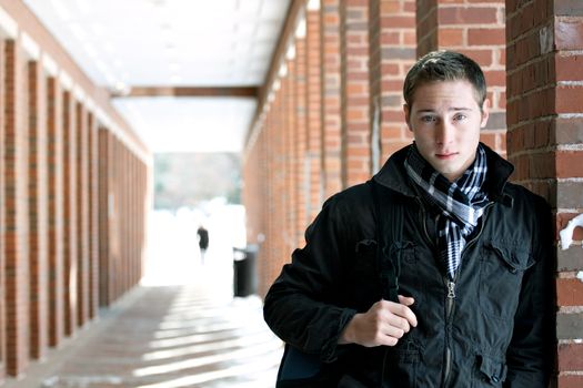 A portrait of a young man standing in an outdoor corridor with his backpack.