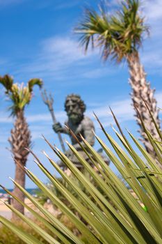 The large public statue of King Neptune in Virginia Beach.  Shallow depth of field with sharp focus on the green tropical foliage.