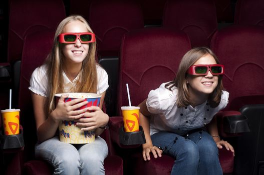 two girls look three-dimensional cinema, sitting in the glasses, eat popcorn, drink drink