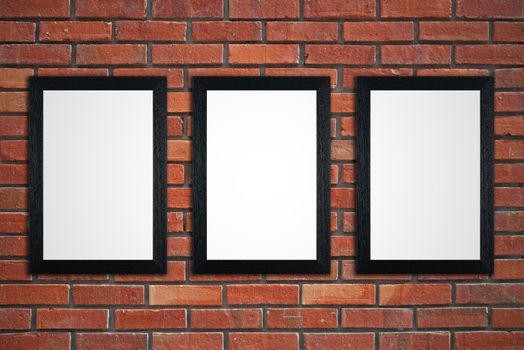 Three black picture frames on red brick wall.