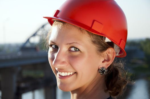 Young architect-woman wearing a protective helmet standing on the bridge background is smiling