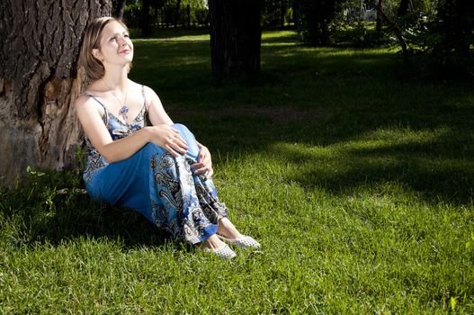 beautiful woman sitting under a tree in park and smiling