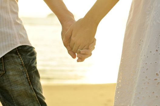 Young adult male and female holding hands on beach at sunset.