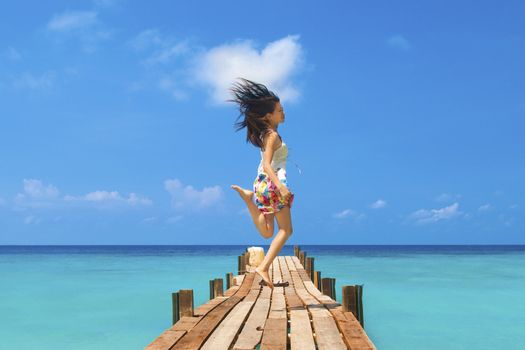 Pretty young girl is jumping up in the air at the beach jetty