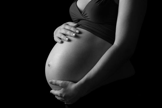 Photo of a pregnant female with her hands on her belly done in black and white.