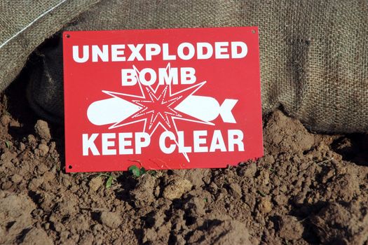 Unexploded Bomb sign next to sand bags and soil