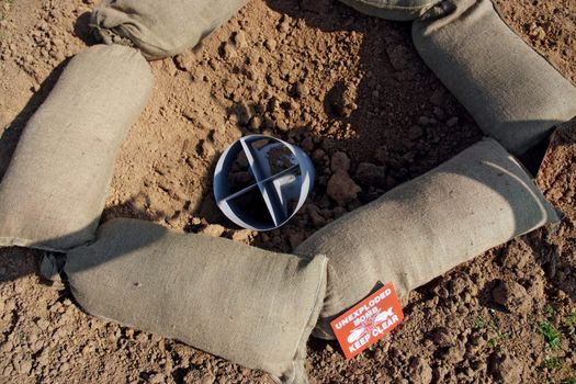 Bomb crater and unexploded bomb with warning signs and sandbags