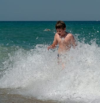 Young boy jumping into wave on a sunny beach