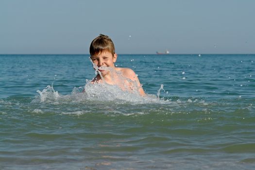 Young boy jumping into wave on a sunny beach 