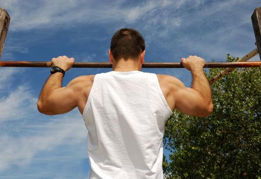Reaching Goal: Strong Man Doing Pull-ups on a Bar in a Park