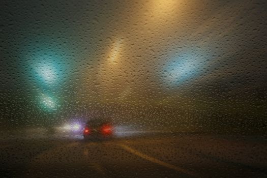 Rainy winter evening on the road with limited visibility seen through a windshield.