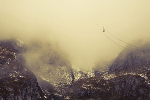 Cable car going up into the low hanging clouds in Pass of Pordoi - Dolomites, Italy. Cross processed and a little filmgrain added to reflect age. Space for text.