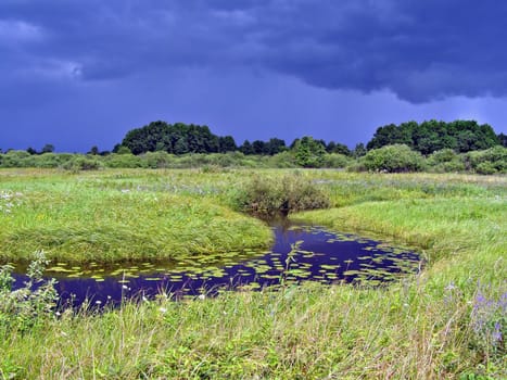 river on field before thunderstorm