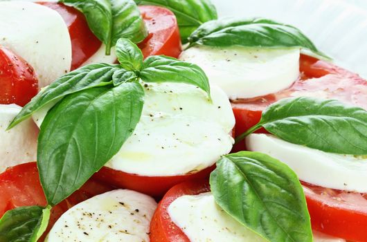 Caprese Salad prepared with mozzarella cheese, fresh organic basil, and tomatoes and then seasoned with olive oil, salt and cracked pepper. 