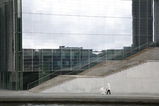 Mother walking with pram in front of the the futuristic library and office building of the German Parliament - Berlin, Germany