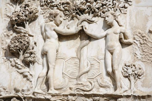 Adam and Eve in the Garden of Eden in front of the tree of knowledge. Detail from the ornate of the facade - Orvieto Cathedral, Umbria, Italy