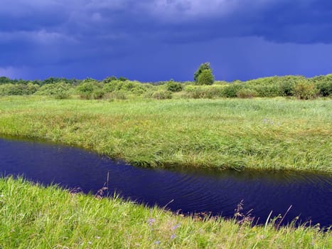 small river on green field before thunderstorm