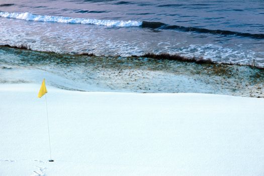 a snow covered links golf hole in ireland in winter weather with yellow flag