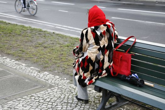 Senior female in fur coat sitting on bench Unter den Linden looking at the traffic - Berlin, Germany