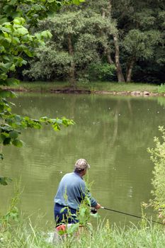 mature man fishing by a river on a beautiful day surrounded by beautiful trees