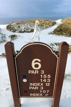 a crystal glass slipper on a hole marker sign in a snow covered irish golf course for a concept on ladies golf