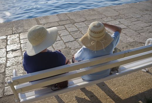 Two elderly females sitting and enjoying their vacation on a bench in the sun - Croatia.