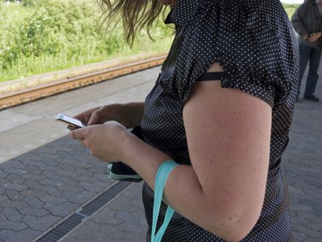 Young girl writing a text message while standing on platform waiting for the train - Nyborg, Denmark.