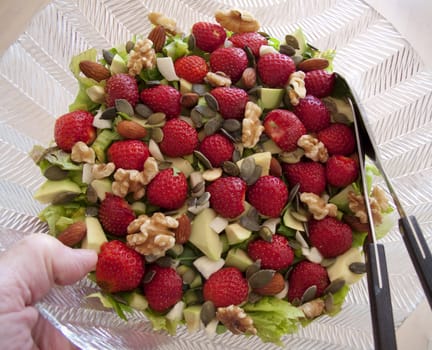 Nice bowl of summer salad with strawberries and nuts beeing served. 