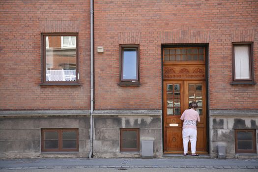 Senior female cleaning the frontdoor of an old weathered urban apartment building.