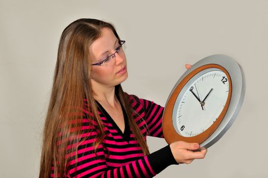 A young girl holding a wall clock against a gray background
