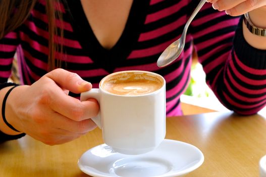 Females holding a cup of cappuccino and a spoon in the other hand