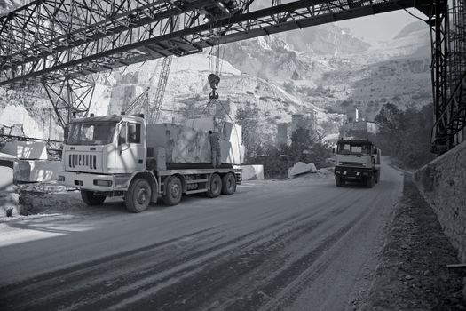 Marble quarry in the mountains near Carrara - Tuscany - Italy. A lorry is being loaded with big blocks of marble for transport whie another one is passing.