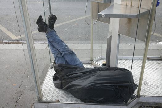 Homeless man sleeping i telephonebox - Paris - France.