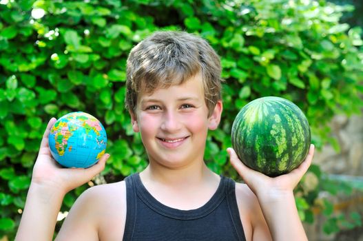 A boy holding a globe and a watermelon shows the difference in size