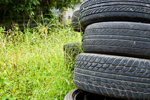 Old road tires stacked on grass land as background

