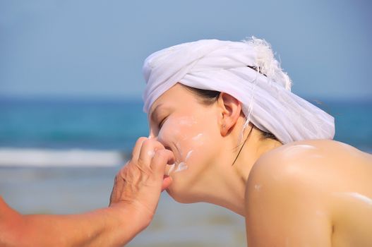 Mother's hand rubs sunscreen on his face against the daughters of a sea view