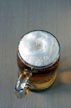 The full glass with foaming beer costs on a wooden table. The top point of shooting.