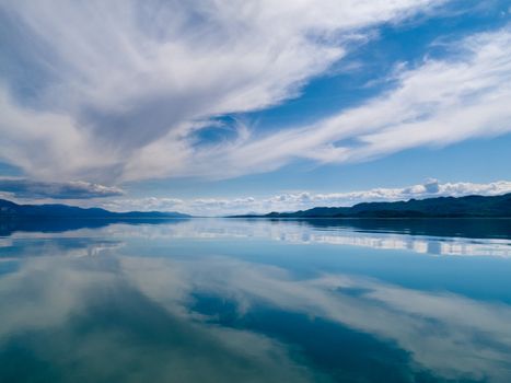 Wild clouds over Lake Laberge, Yukon Territory, Canada, are mirrored on water surface on beautiful summer day.