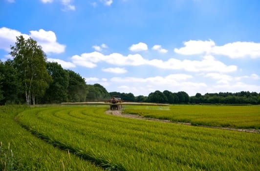 bright green agriculture farmland with tractor sprinkle-sweeper installation with cloudy blue sky
