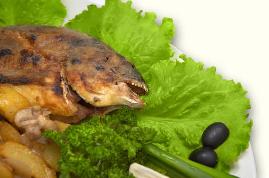 close-up: whole grilled dorada fish, with baked potato, mushrooms and fresh vegetables, served on the plate with lettuce leaves and with lemon slice.