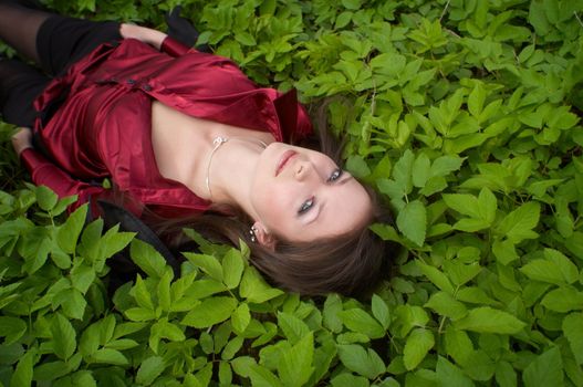 sexy brunette in red laying on green foliage