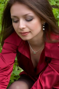 sexy brunette in red sitting on the green foliage