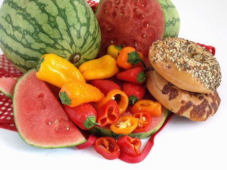 Beautiful red, orange and yellow peppers, ripe watermelon, and bagels set against a white background.