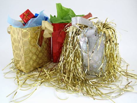 Shiny foil gift bags full of wrapped presents. Decorated with gold tinsel over a white background.