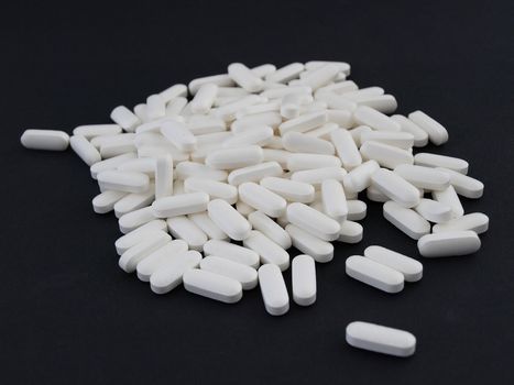 A spill of large white pills over a black background.